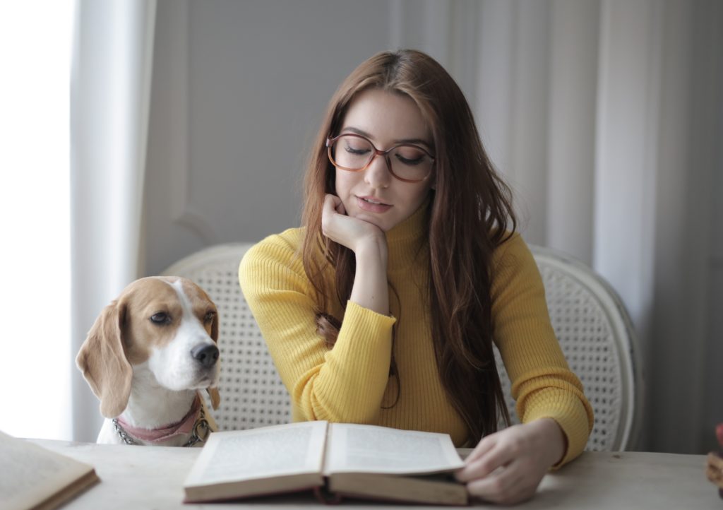 A woman reads her book next to her dog. 